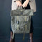 Person holding an olive green NOEL rolltop backpack made in Europe, styled with a taupe jacket and brown boots.