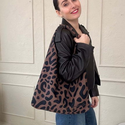 Woman in a stylish black leather jacket holding a trendy leopard print tote bag.
