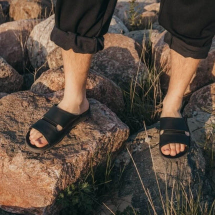 Men's handmade black sandals on rocky terrain, offering everyday comfort and stylish design.