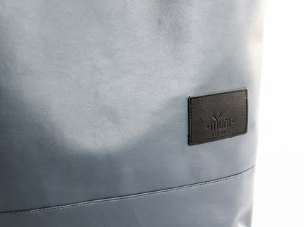 Close-up of grey faux leather backpack with black logo label, showcasing modern and stylish design.