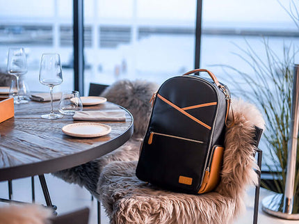 Large Black Coffee Diaper Backpack resting on a chair with a modern dining setting and waterfront view.