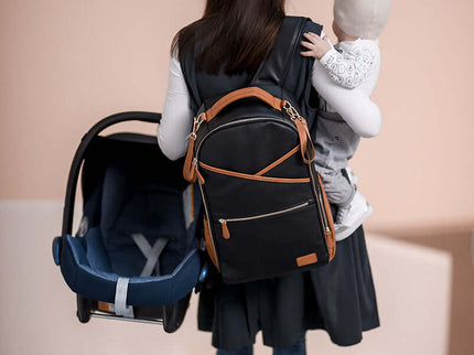 A parent carrying a large black diaper backpack and a baby while navigating stairs.