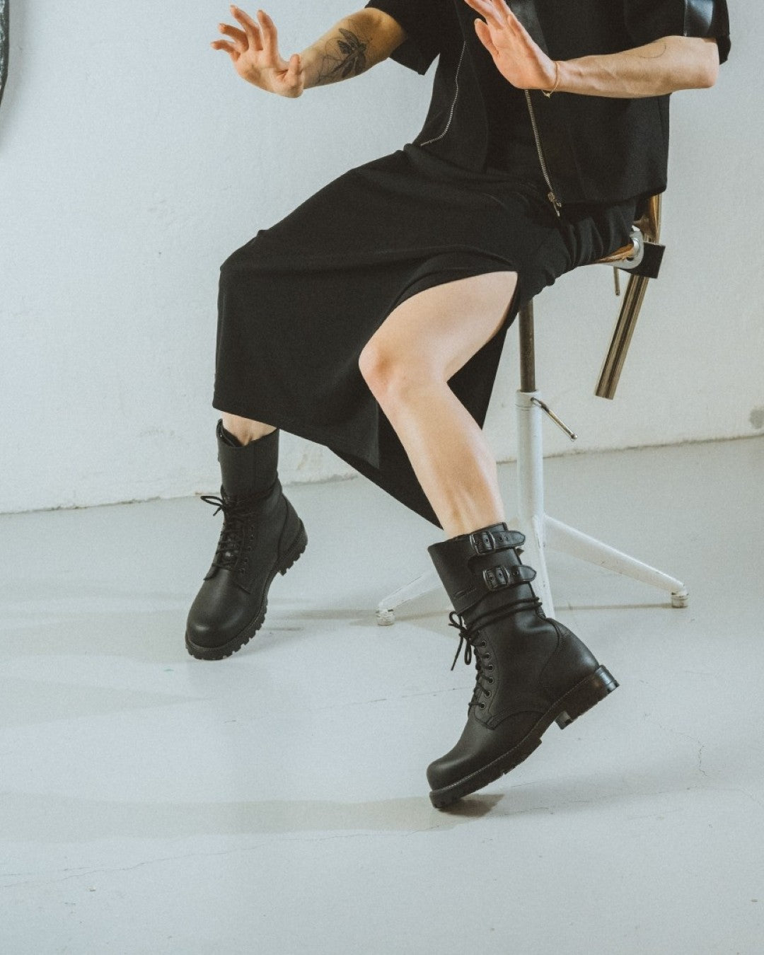 Person wearing black boots sitting on a chair against a white background
