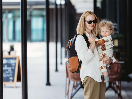 Stylish parent holding a child while carrying a large black coffee diaper backpack.
