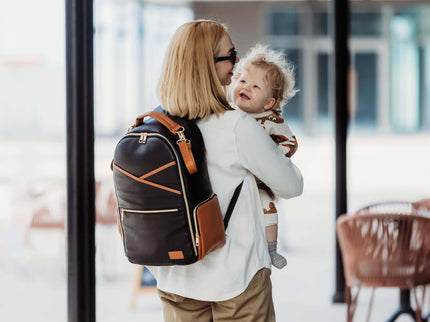Parent carrying a child while wearing a stylish black coffee diaper backpack outdoors.