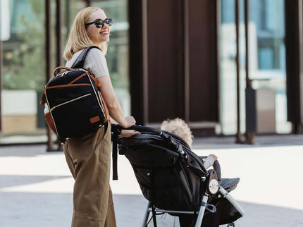 Stylish parent with Small Diaper Backpack in Black Coffee pushing a stroller on urban street.