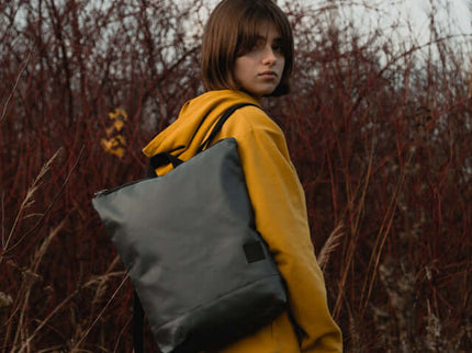 Young person wearing a grey faux leather backpack outdoors, styled with a yellow hoodie.