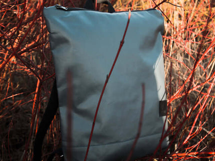 Grey faux leather backpack in an outdoor setting with vibrant foliage.