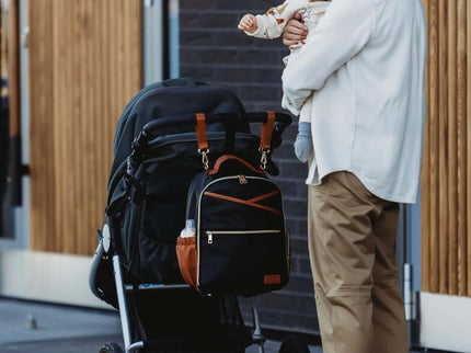 Stylish mom carrying a baby with a Small Diaper Backpack – Black Coffee beside a stroller, showcasing versatility and elegance.