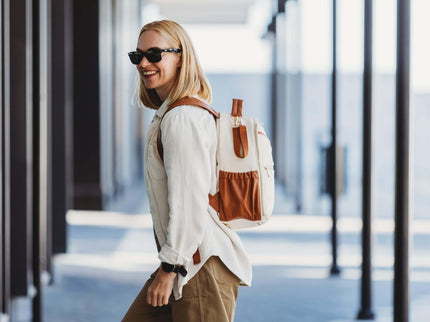 Stylish woman wearing a Cappuccino Small Diaper Backpack, smiling in a modern urban setting.