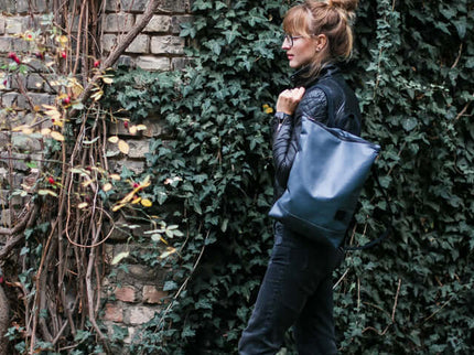 Woman wearing a grey faux leather backpack against an ivy-covered brick wall, showcasing a trendy street style.