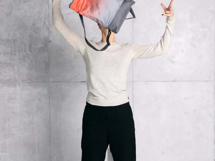 Trendy salmon and gray faux leather backpack held by a person in a casual outfit, showcasing a stylish urban look.