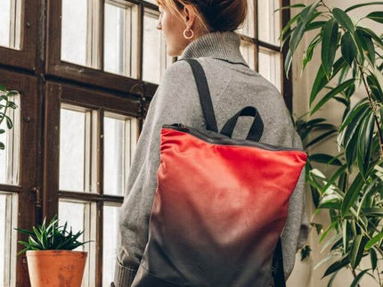 Stylish salmon faux leather backpack worn by a woman in a cozy gray sweater, showcasing its trendy gradient design.