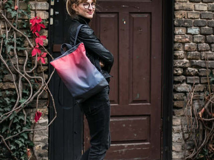 Woman wearing a stylish salmon faux leather backpack against an urban brick backdrop.
