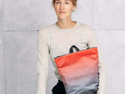 Model holding a salmon and gray faux leather backpack, showcasing its stylish design against a minimalist background.