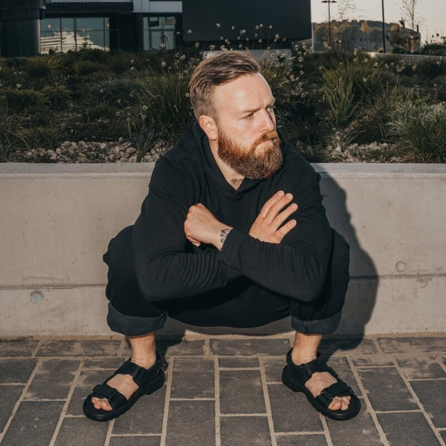 Man squatting outdoors in Lauri Leather Sandals, showcasing sporty design and outdoor comfort.
