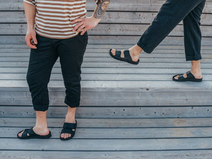 Two individuals wearing Märt Black Leather Sandals on wooden steps, showcasing everyday comfort and style.