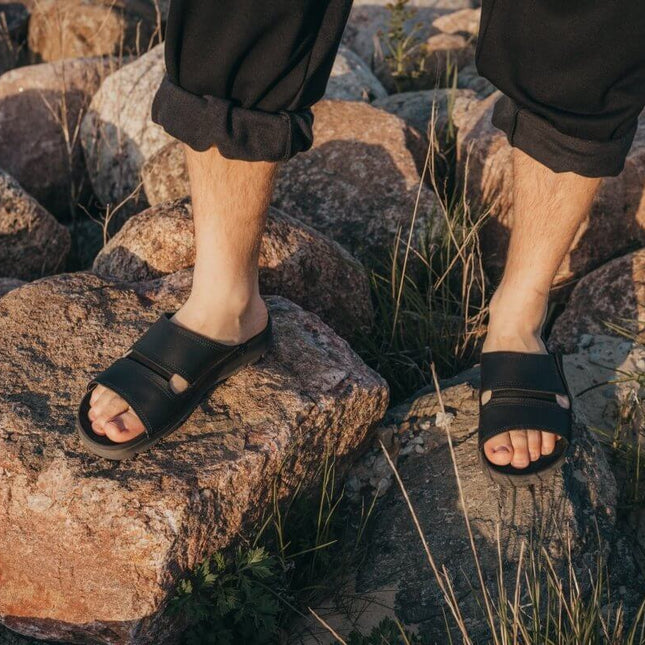 Miku Sandals in black worn outdoors on rocky terrain, showcasing minimalist design and comfort.