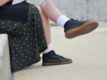 Person wearing TOKU Stockholm sustainable sneakers, reading a magazine while sitting on a concrete ledge.