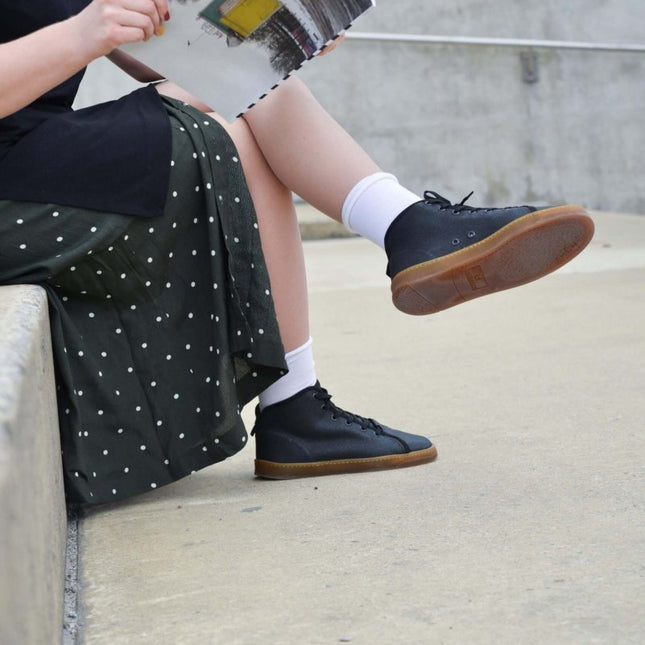 Person wearing TOKU Stockholm sustainable sneakers, reading a magazine while sitting on a concrete ledge.
