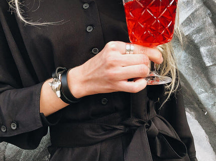 Woman wearing a black outfit holding a glass of red drink with a stylish bracelet on her wrist.