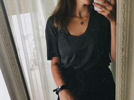 Woman taking a mirror selfie in a black shirt showcasing stylish accessories.